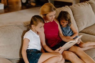 uma mulher e duas jovens sentadas em um sofá lendo um livro