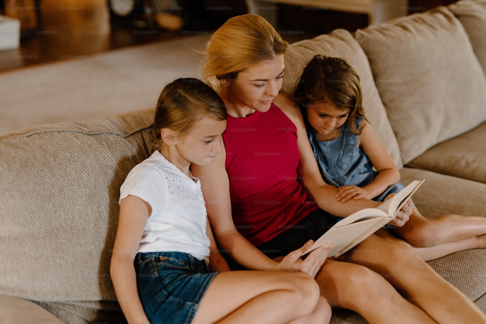 a woman and two young girls sitting on a couch reading a book