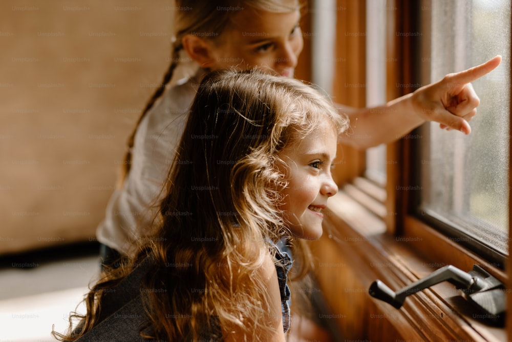 Ein kleines Mädchen, das aus einem Fenster auf ein anderes kleines Mädchen zeigt