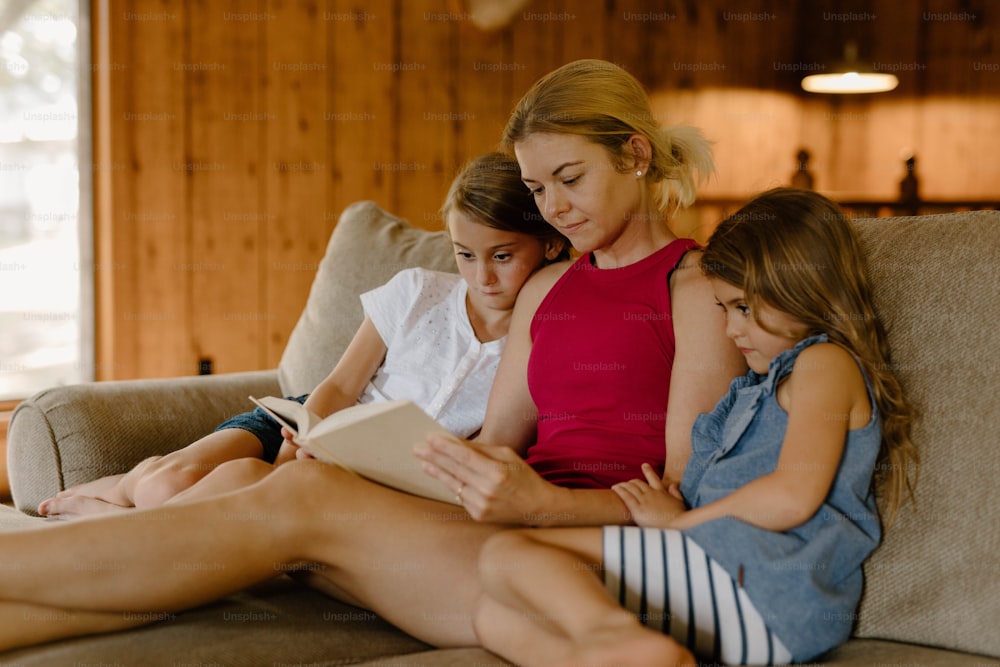 three girls sitting on a couch reading a book