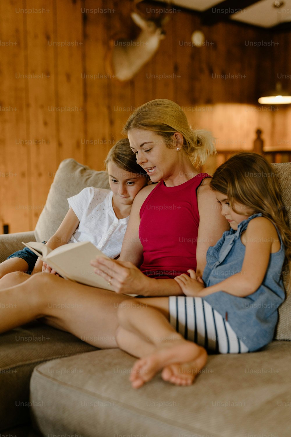 a woman and two girls sitting on a couch reading a book