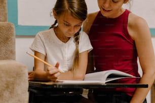 uma mulher e uma menina sentadas em uma mesa com um livro e lápis