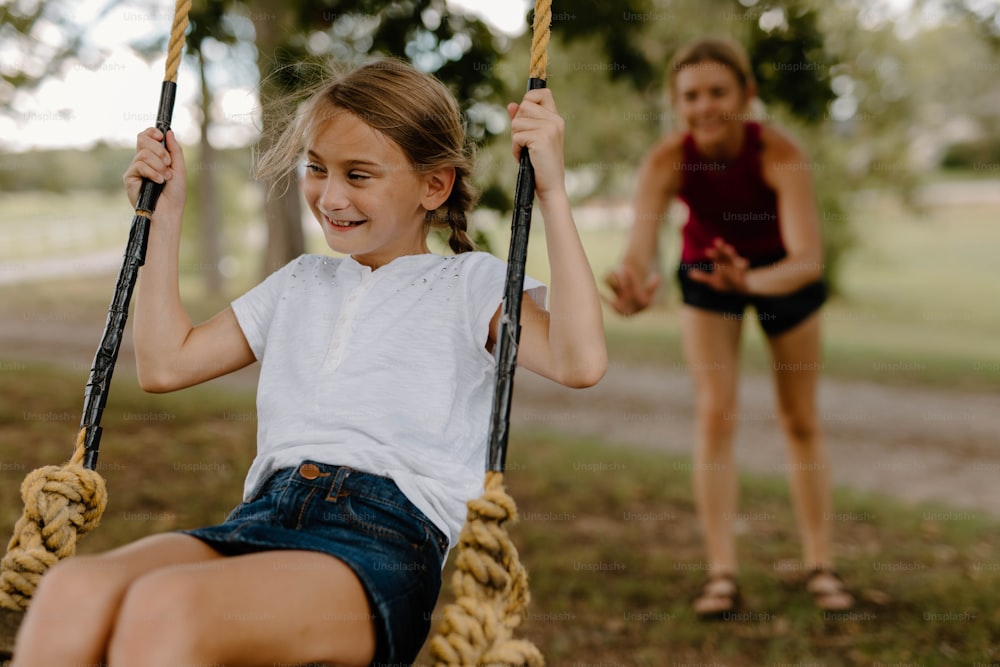 a girl sitting on a rope swing next to a woman