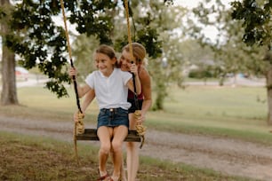 two girls sitting on a swing in a park