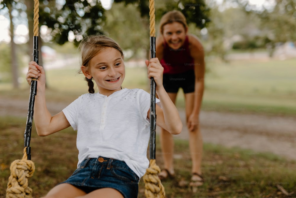 a little girl sitting on a rope swing next to a woman