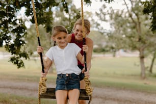 two girls sitting on a swing in a park