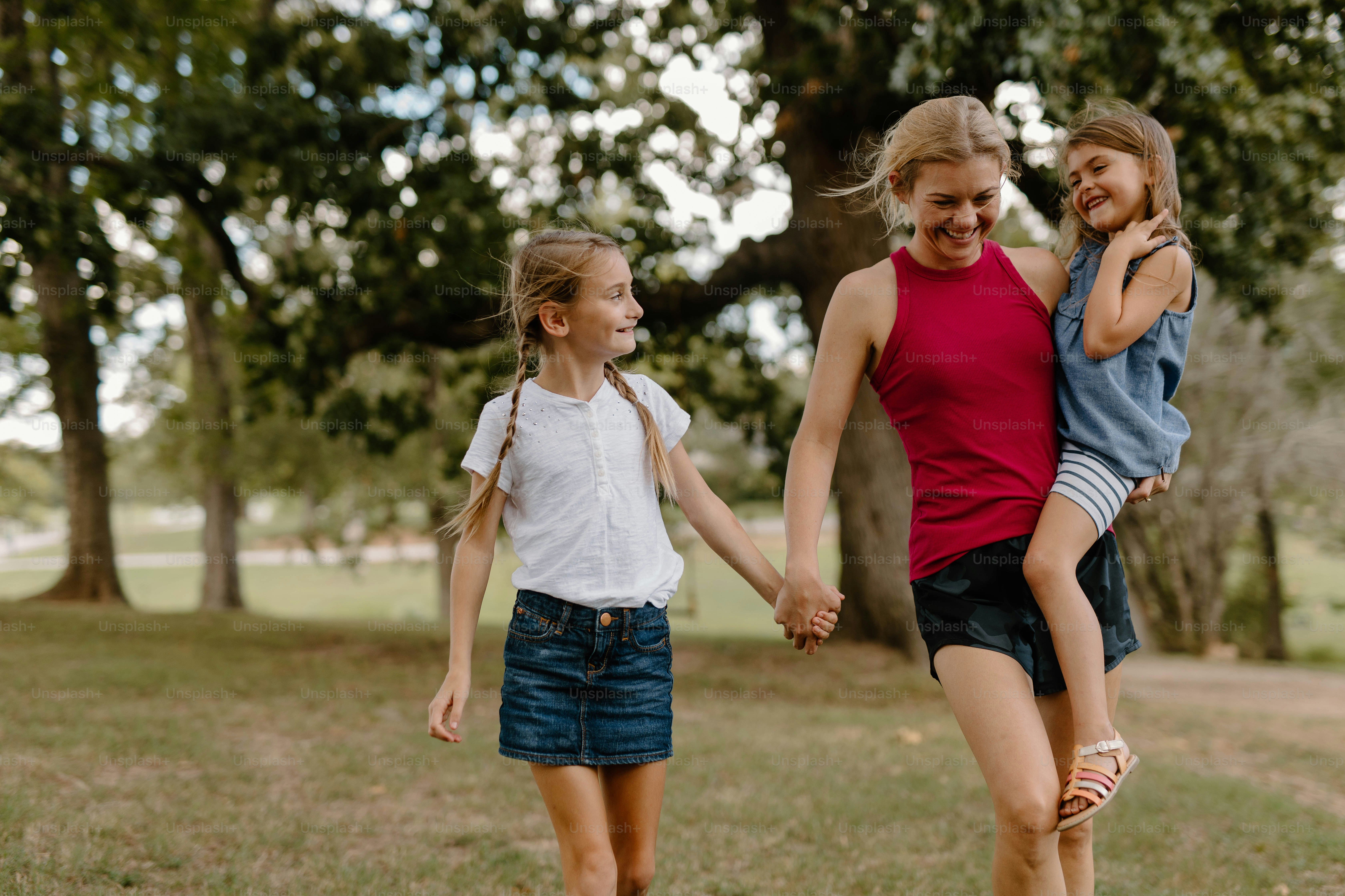 two girls holding hands and walking in a park
