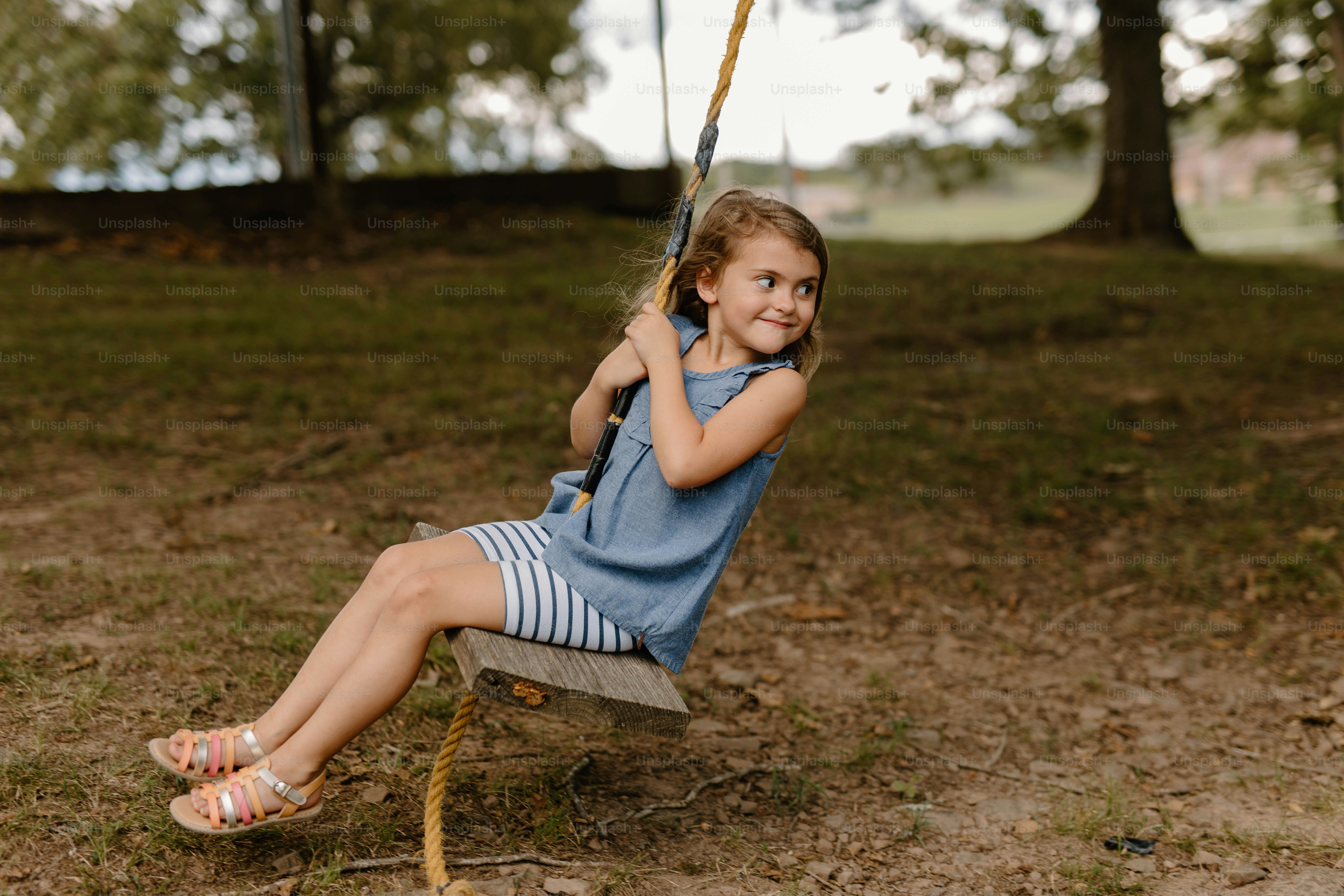 a little girl sitting on a swing in a park