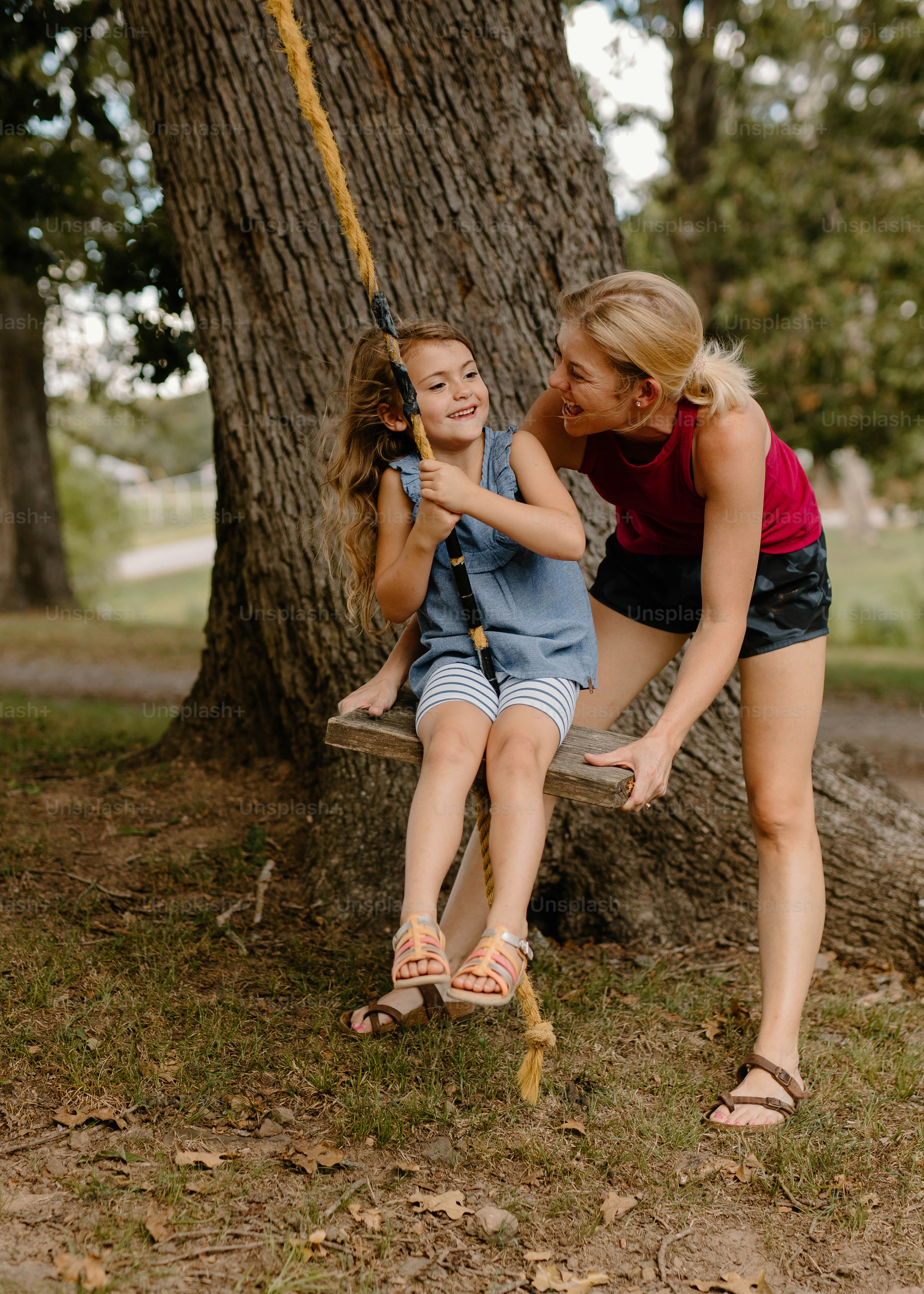 two girls sitting on a swing in a park