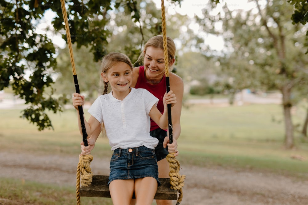 a woman and a little girl sitting on a swing