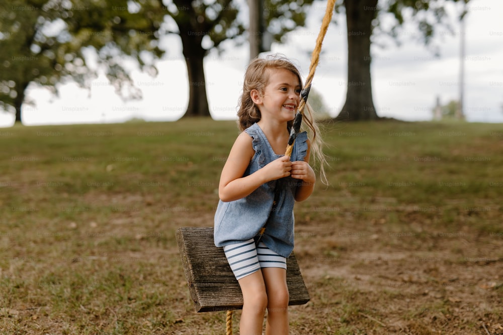 a little girl sitting on a swing in a park