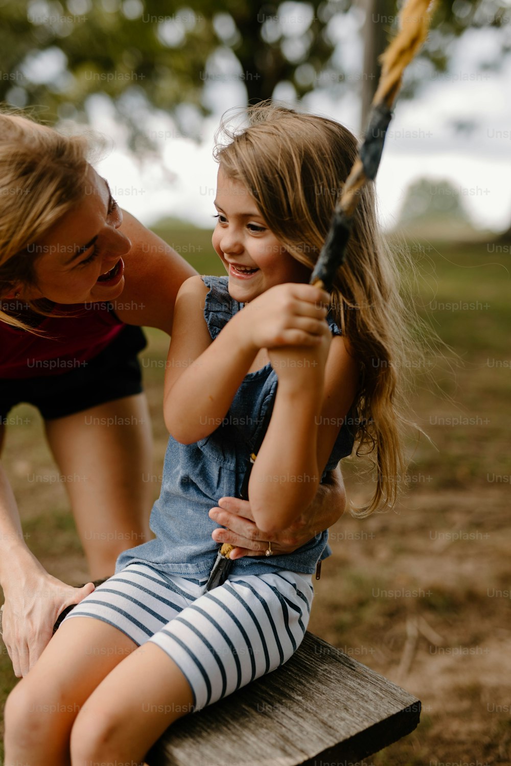 a young girl sitting on top of a wooden bench next to a woman