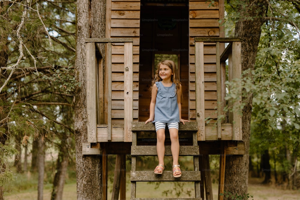 a little girl sitting on a wooden tree house