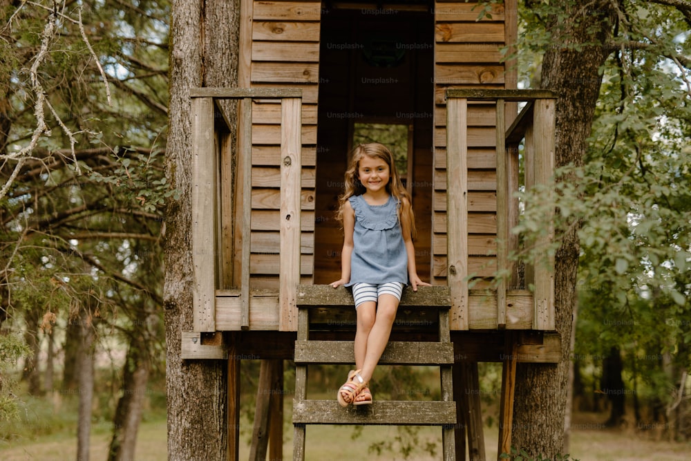 a little girl sitting on a wooden tree house