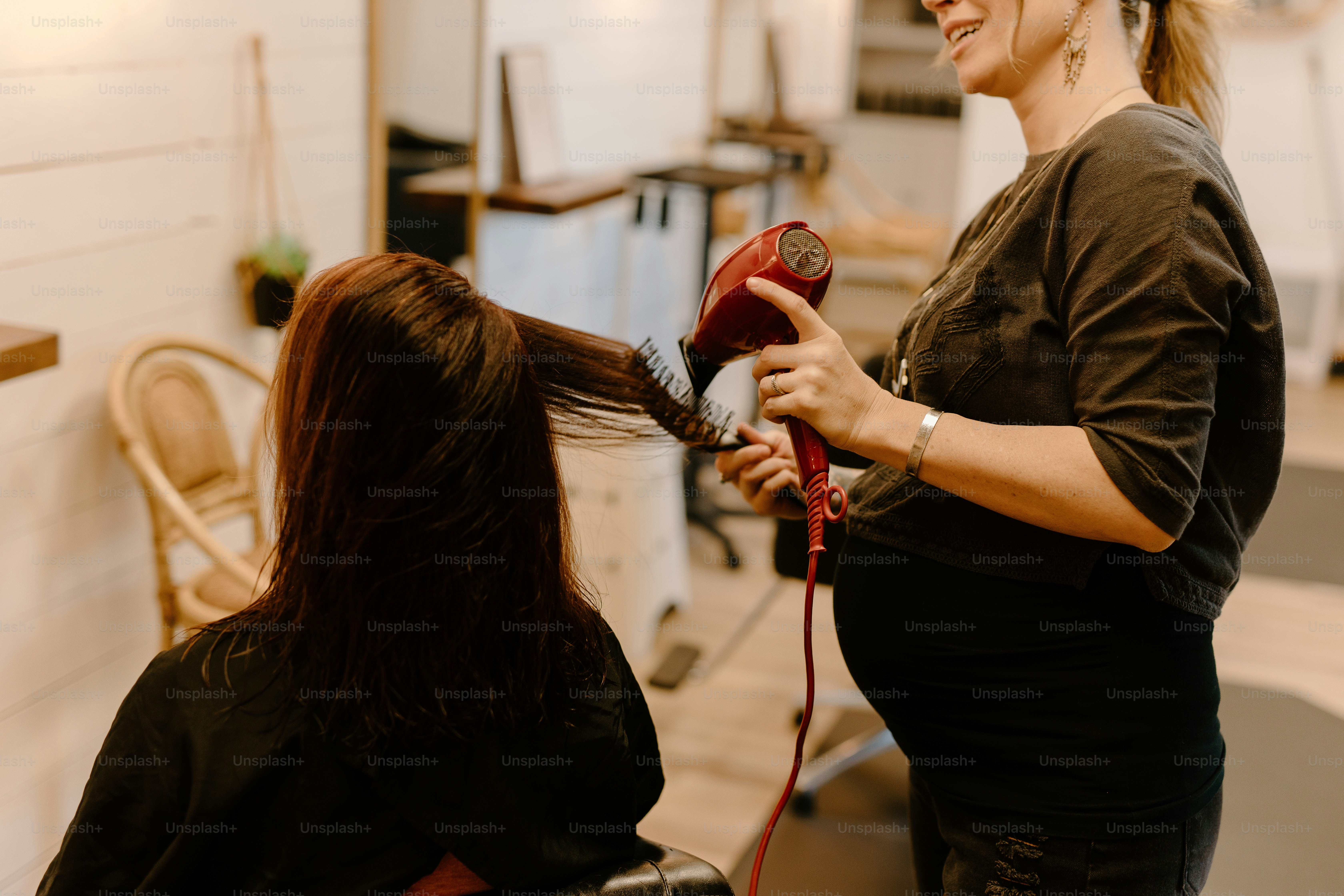 a woman is blow drying another woman's hair