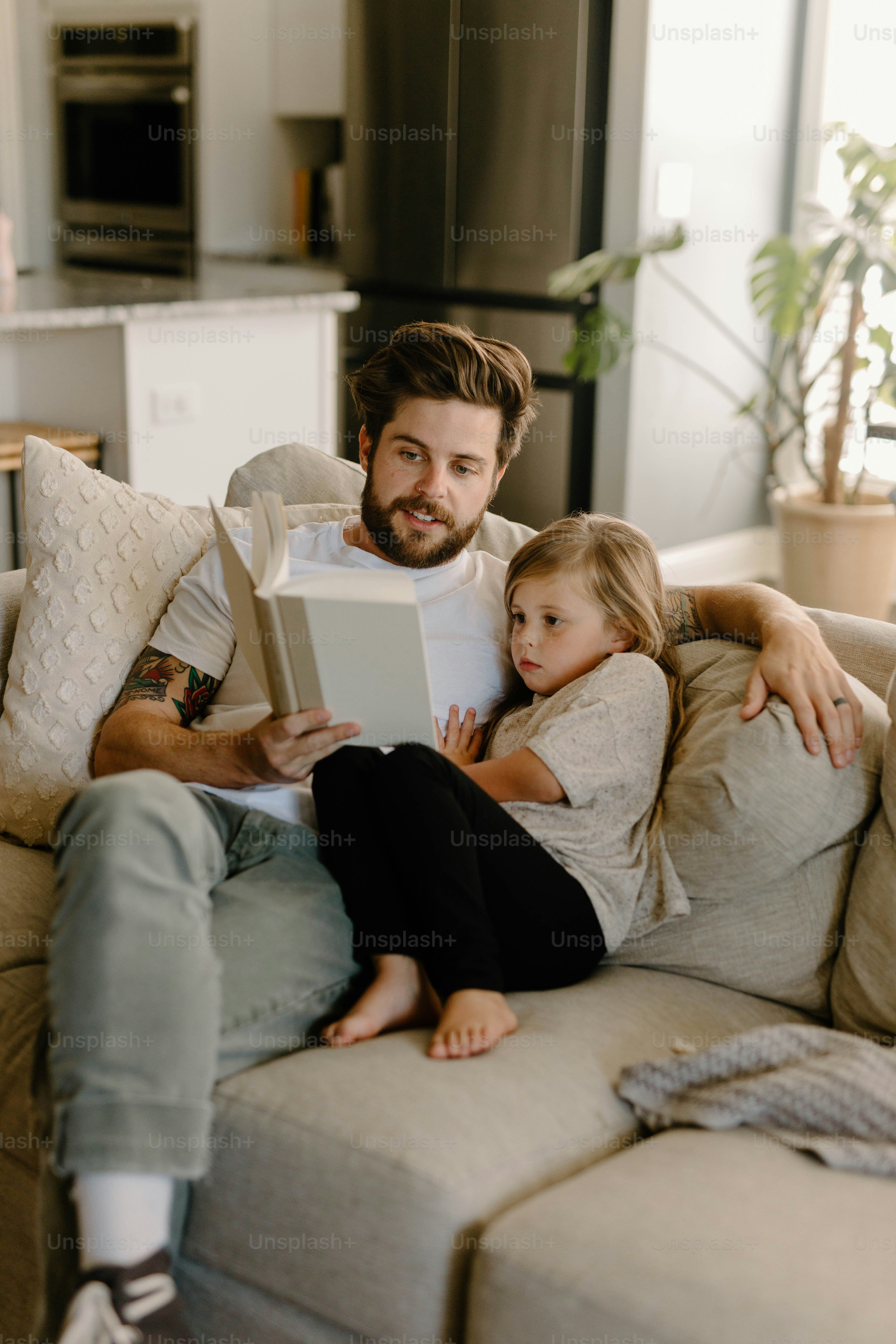 a man sitting on a couch reading a book to a little girl