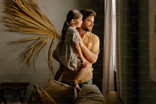 a man holding a little girl while standing next to a window