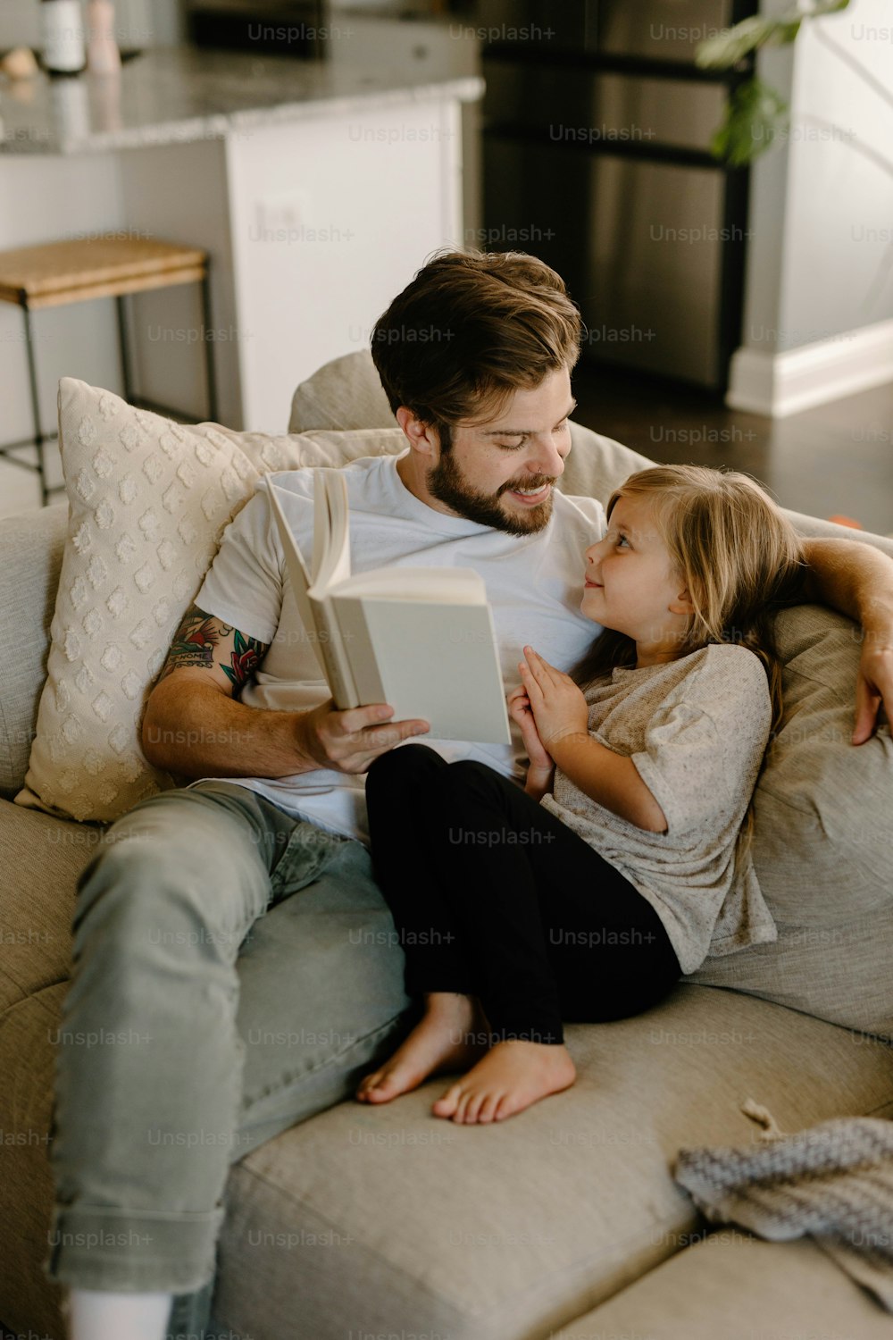 소파에 앉아 어린 소녀에게 책을 읽어주��는 남자