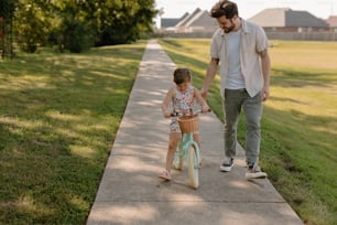 a man and a little girl riding a bike down a sidewalk