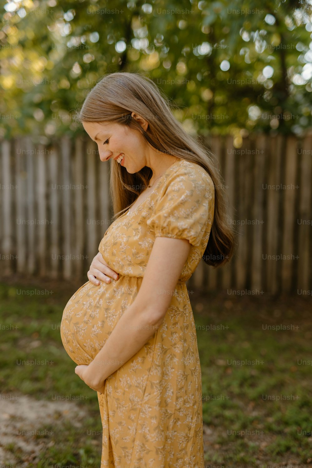 a pregnant woman in a yellow dress standing in front of a fence