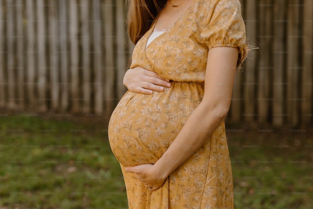 a pregnant woman in a yellow dress poses for a picture
