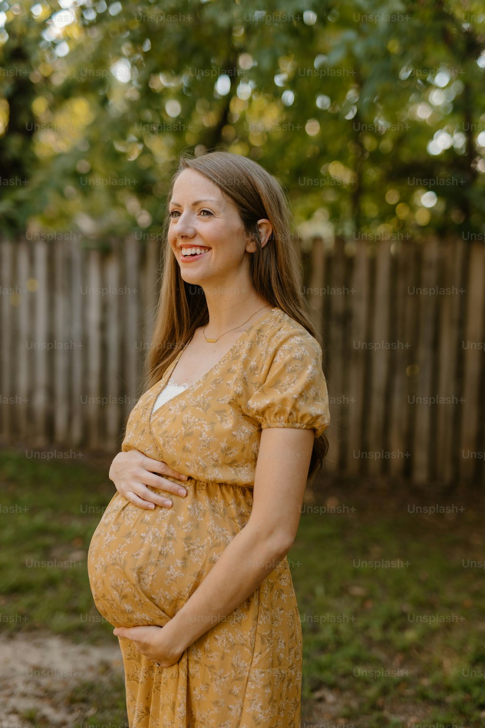 Una mujer embarazada con un vestido amarillo sonríe a la cámara