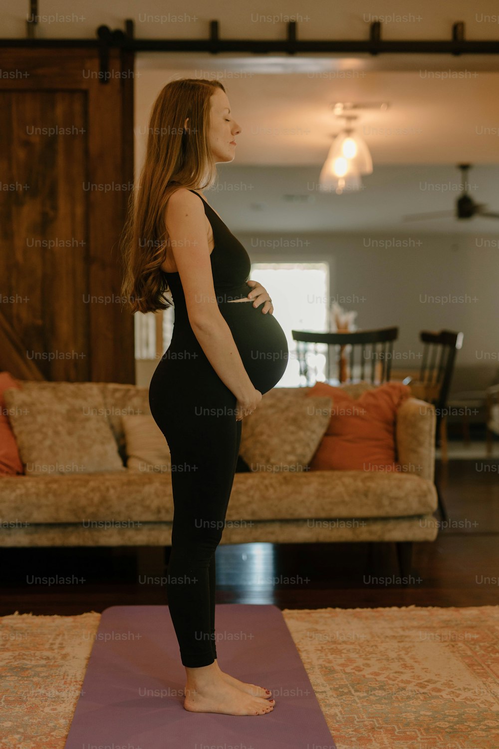 Una mujer embarazada de pie en una esterilla de yoga en una sala de estar
