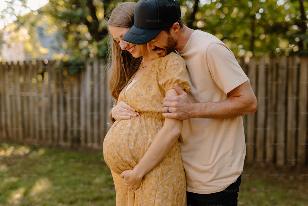 a pregnant couple cuddle in a backyard