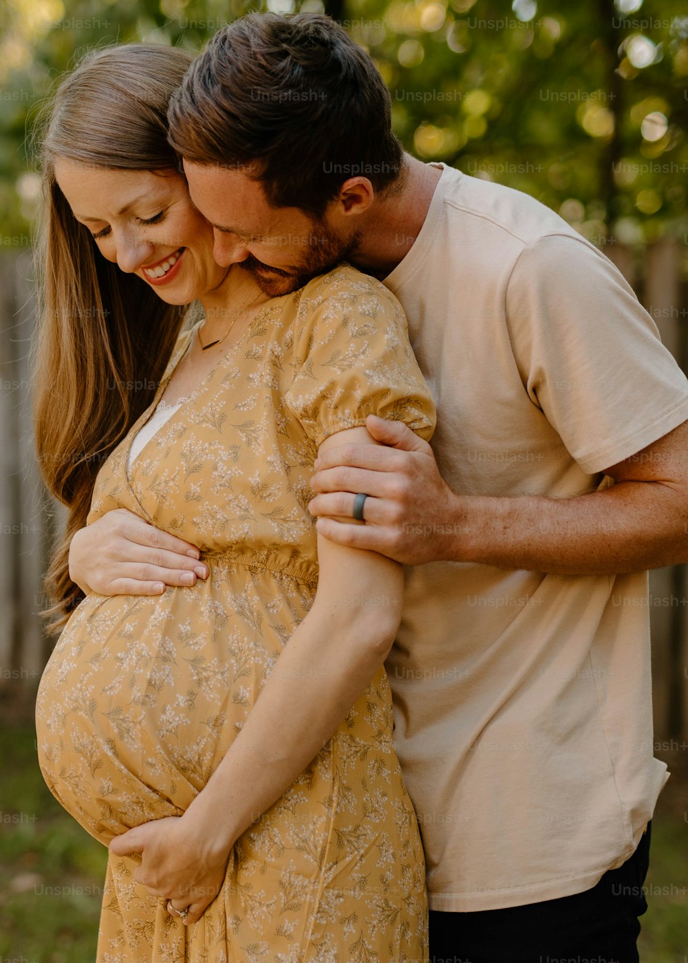 Ein schwangeres Paar, das sich umarmt und in die Kamera lächelt