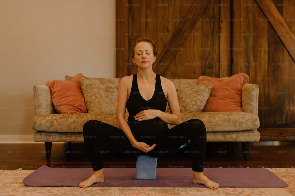 uma mulher grávida sentada em um tapete de ioga em uma sala de estar
