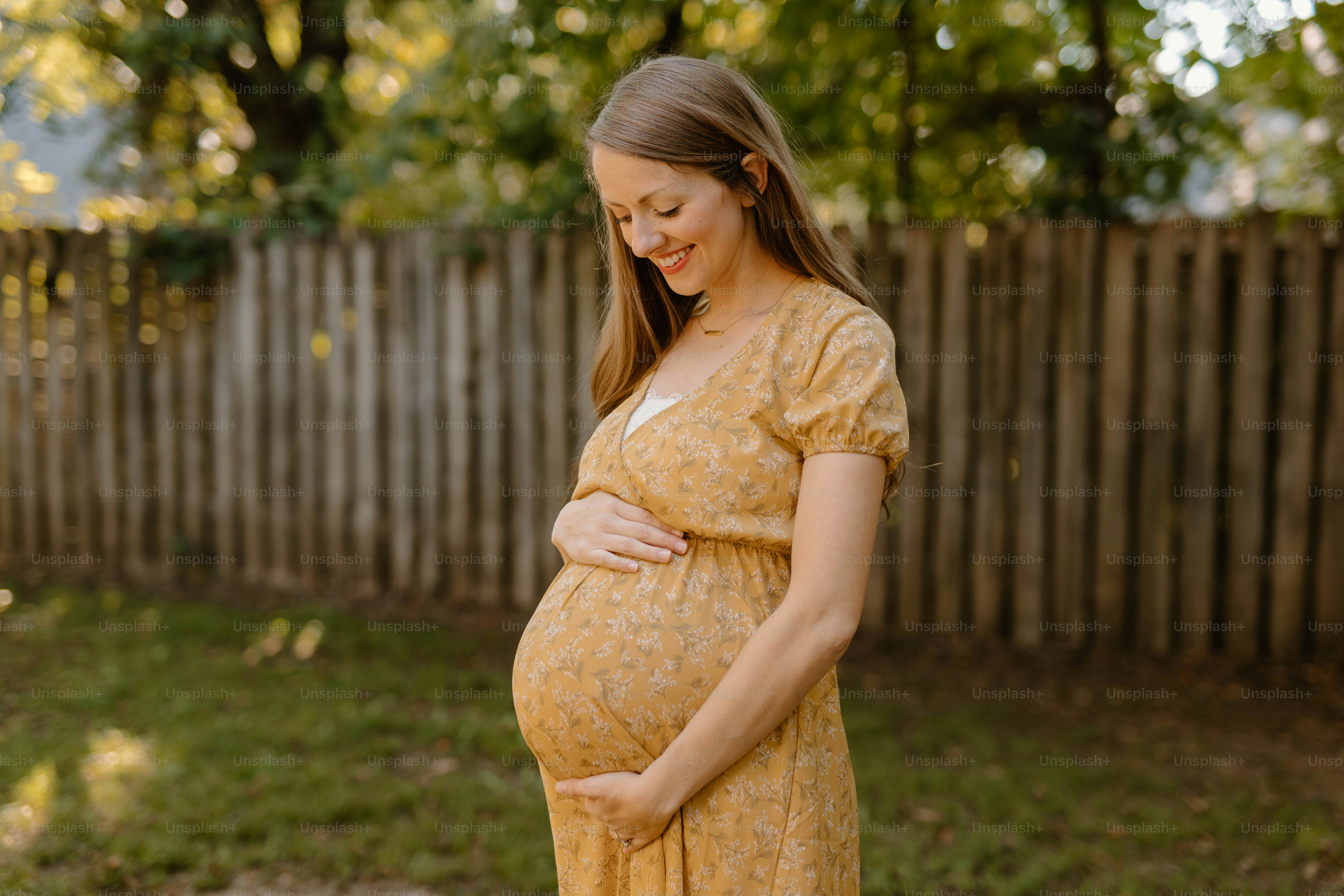 a pregnant woman in a yellow dress standing in a yard