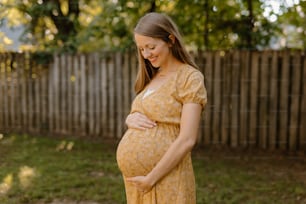 a pregnant woman in a yellow dress standing in a yard
