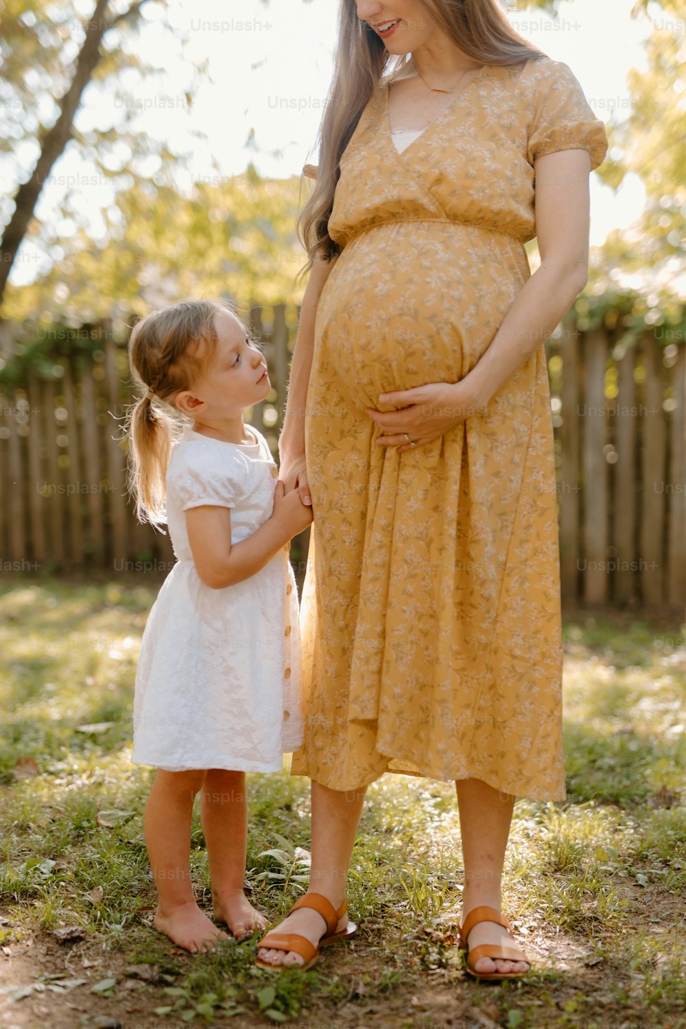 a pregnant woman standing next to a little girl