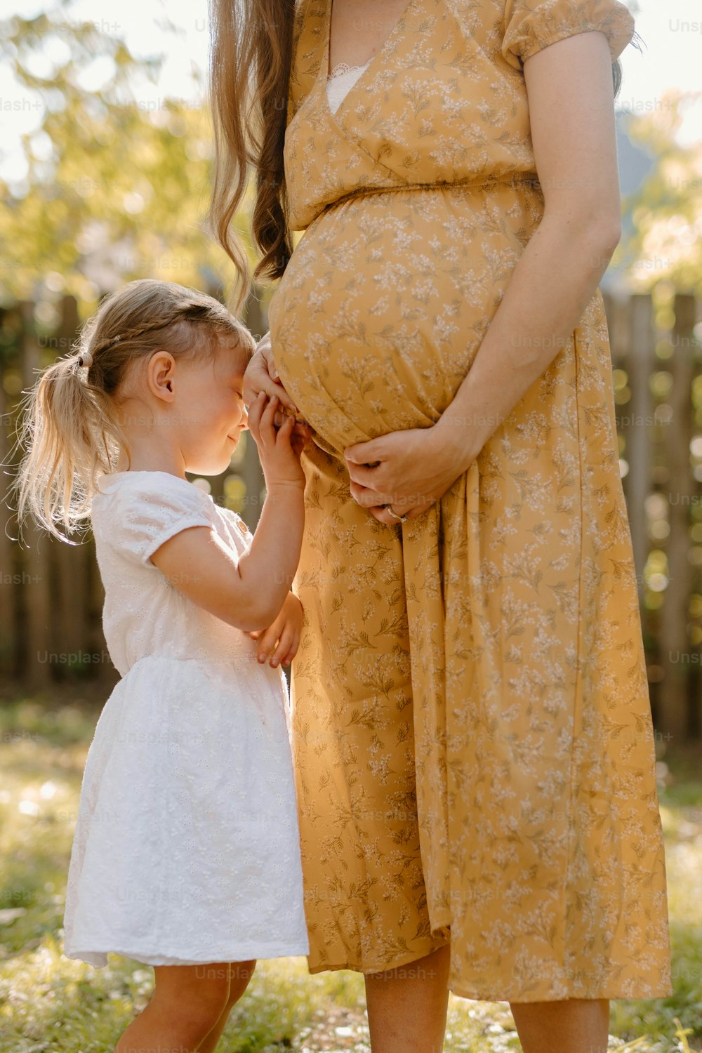 a pregnant woman holding the hand of a little girl