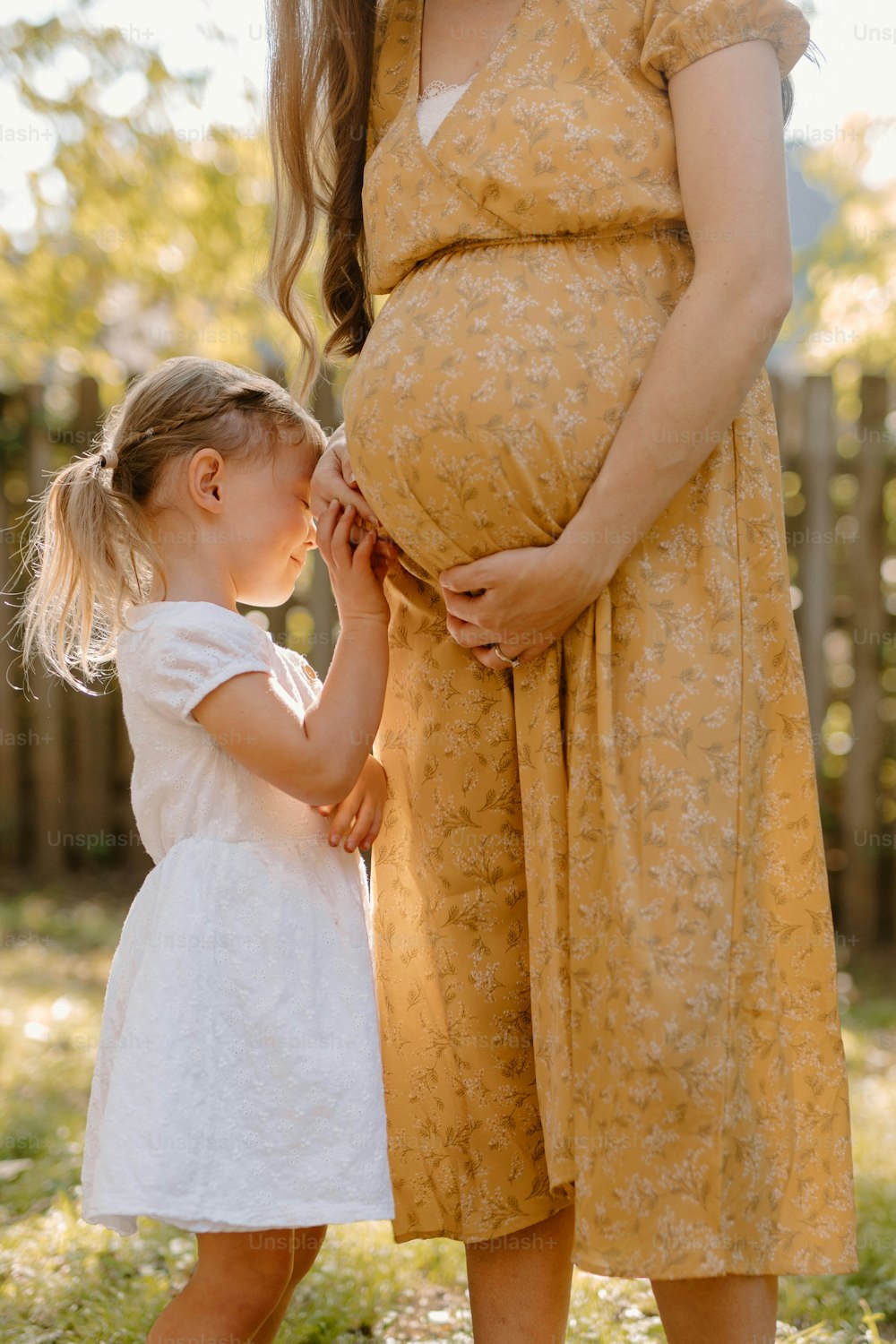 eine schwangere Frau, die die Hand eines kleinen Mädchens hält