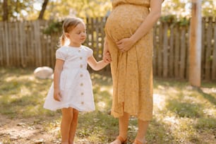 a pregnant woman holding the hand of a young girl