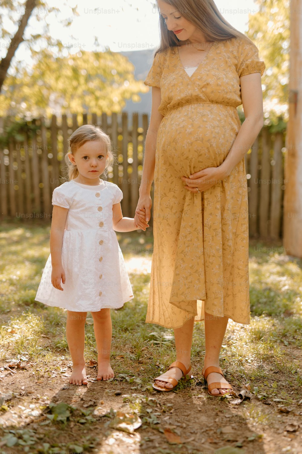 eine schwangere Frau, die die Hand eines kleinen Mädchens hält