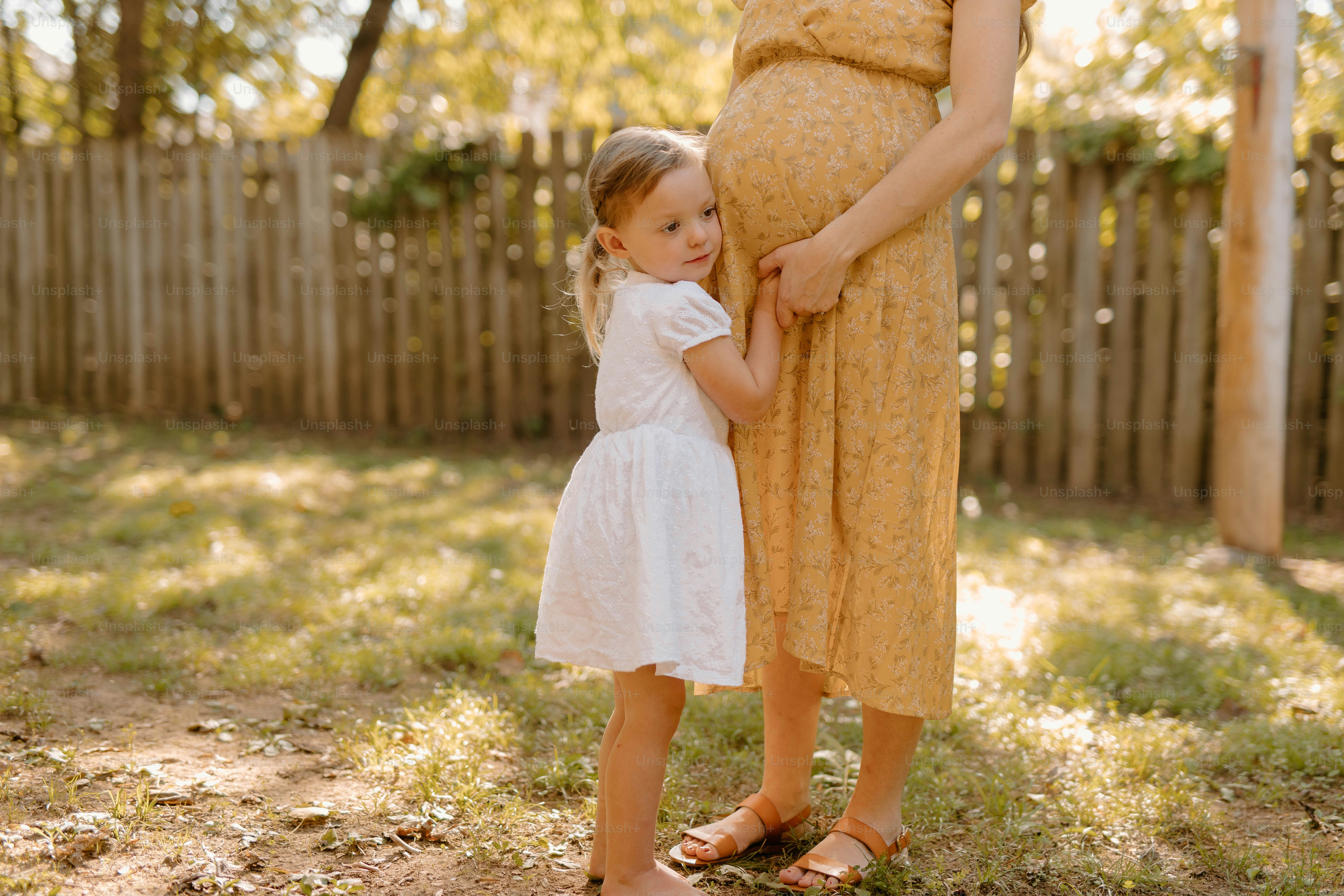 a pregnant woman holding the hand of a little girl