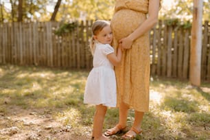 a pregnant woman holding the hand of a little girl