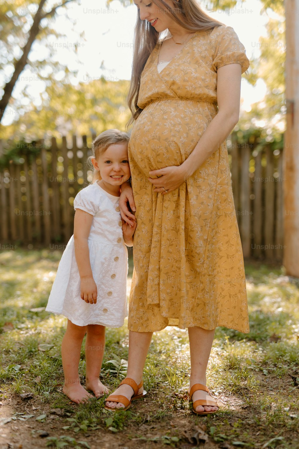 a pregnant woman standing next to a little girl