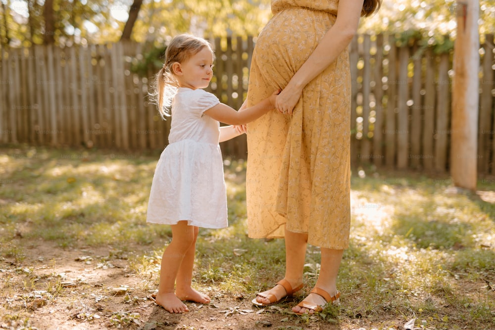 a pregnant woman holding the hand of a little girl