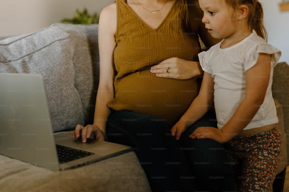 a pregnant woman sitting on a couch next to a little girl