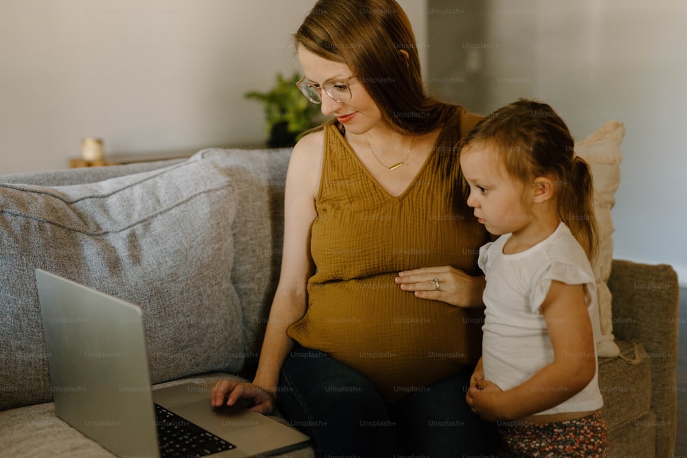 a pregnant woman sitting on a couch next to a little girl