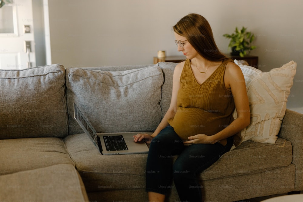 eine schwangere Frau, die mit einem Laptop auf einer Couch sitzt