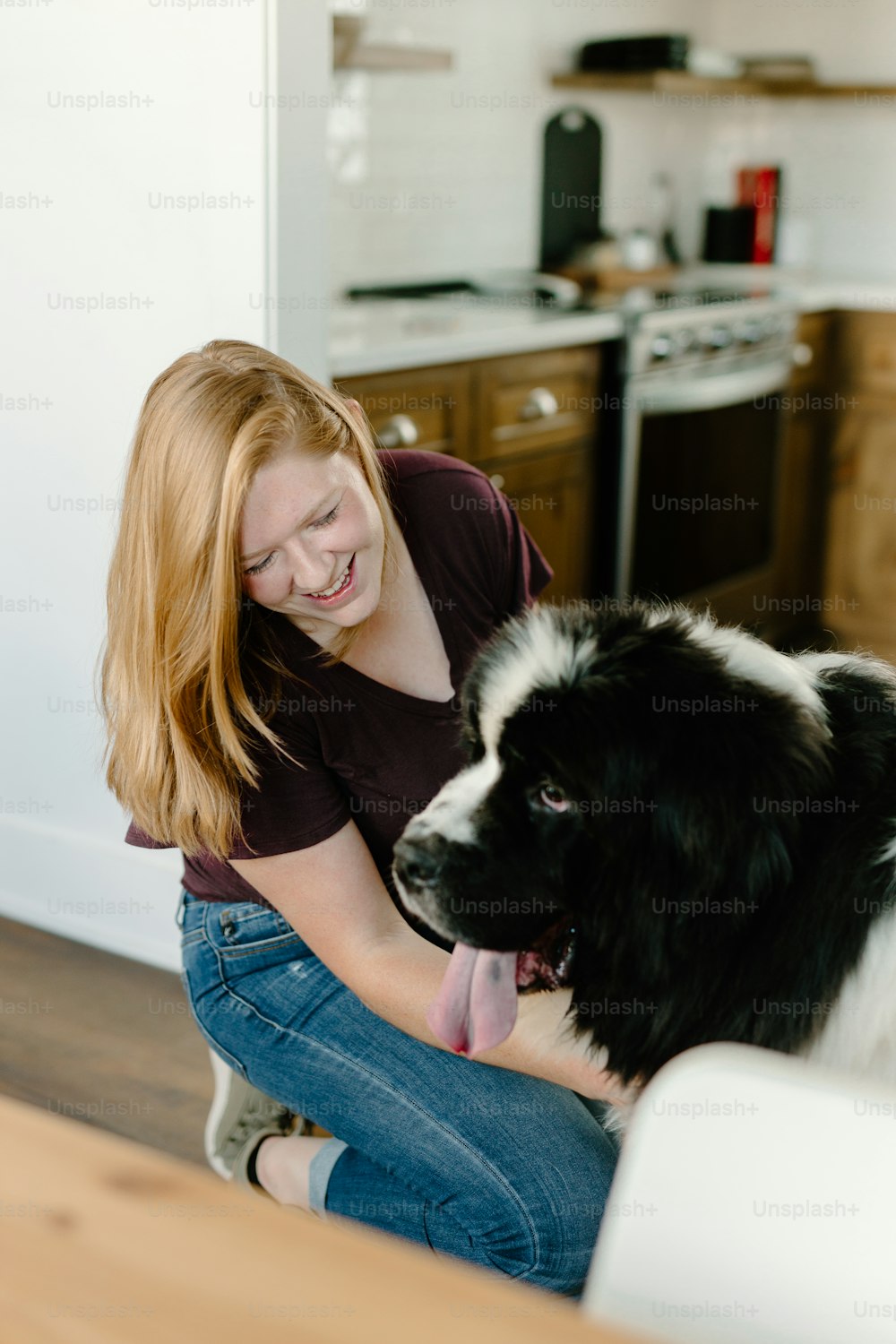 uma mulher acariciando um cão preto e branco em uma cozinha