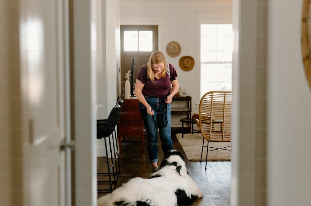 Una mujer parada en una sala de estar junto a un perro blanco y negro