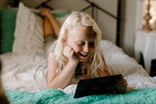 Une petite fille allongée sur un lit regardant une tablette