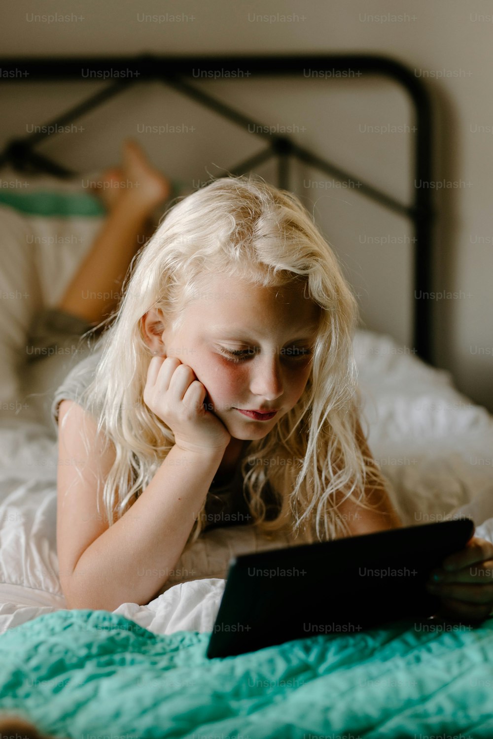 a little girl laying on a bed looking at a tablet