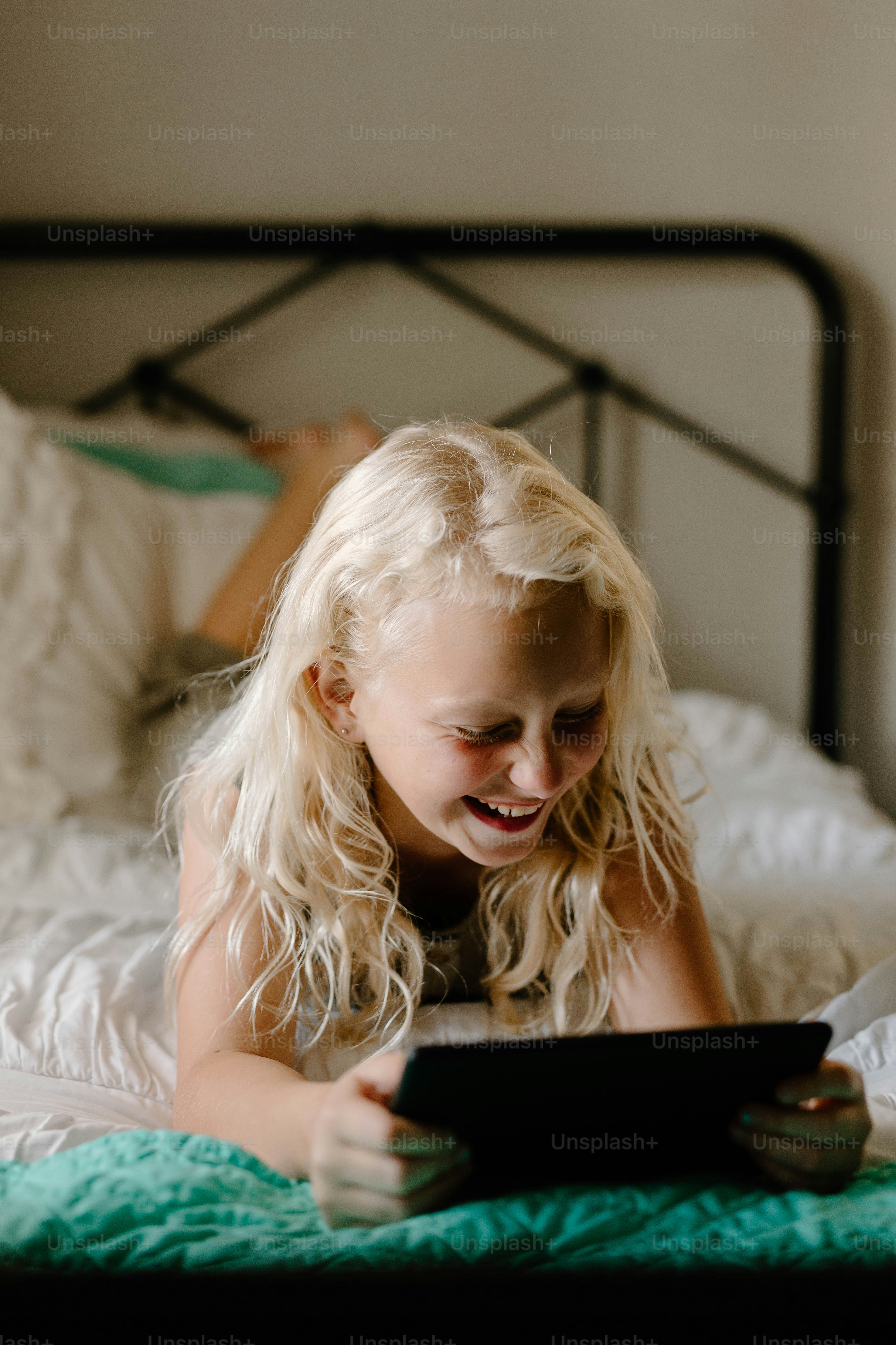 a little girl laying on a bed looking at a tablet