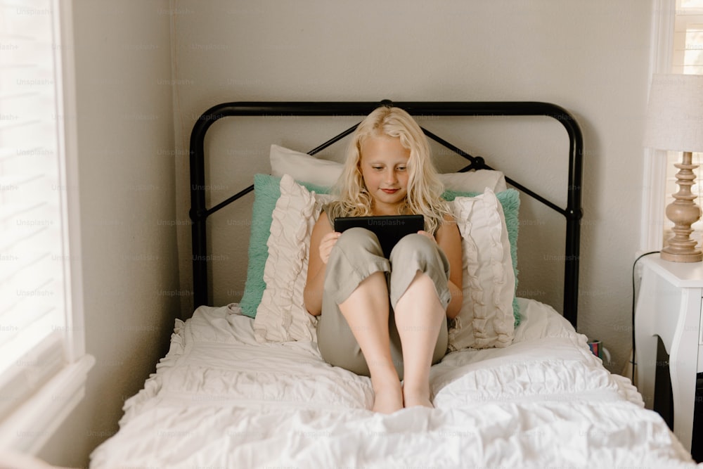 a woman sitting on a bed looking at a tablet